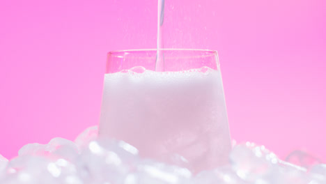Nahaufnahme-Einer-Person,-Die-Gekühltes-Kaltgetränk-Aus-Der-Dose-Auf-Eiswürfeln-Vor-Rosa-Hintergrund-In-Ein-Glas-Gießt